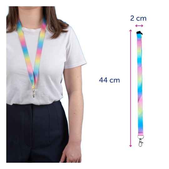 Kuvassa on henkilö, joka käyttää värikästä klipsillä varustettua avainkaulahihnaa. Avainkaulahihnassa on liukuvärjätty pastellivärinen design, ja sen pituus on 44 cm ja leveys 2 cm.