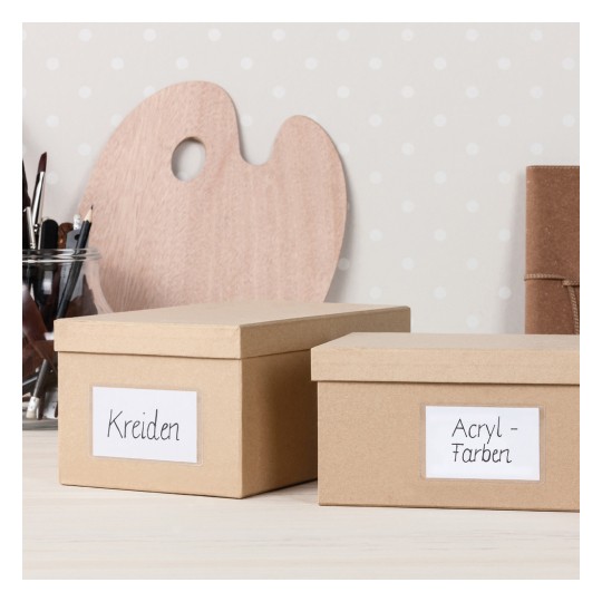 Kuvassa näkyy kaksi merkittyä laatikkoa työtilassa. Yksi laatikko on merkitty 'Kreiden' ja toinen 'Acryl-Farben,' taustalla on puinen paletti ja siveltimiä.