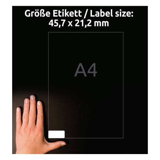 Kuvassa näkyy käsi A4-etiketin vieressä, jonka mitat ovat 45,7 x 21,2 mm. Tausta on tumma, mikä parantaa etiketin ja käden näkyvyyttä.