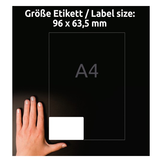 Kuva näyttää käden etiketin vieressä. Etiketin koko on 96 x 63,5 mm, ja sen takana on ilmoitettu A4-koko. Tausta on tumma, mikä parantaa esineiden näkyvyyttä.