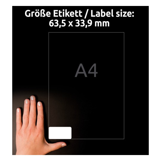 Kuva esittää kättä vierekkäin tarran, jonka koko on 63,5 x 33,9 mm, kanssa, ja kirjain 'A4' on esillä näkyvästi. Tausta on tumma, mikä korostaa tarran kokoa ja kättä.