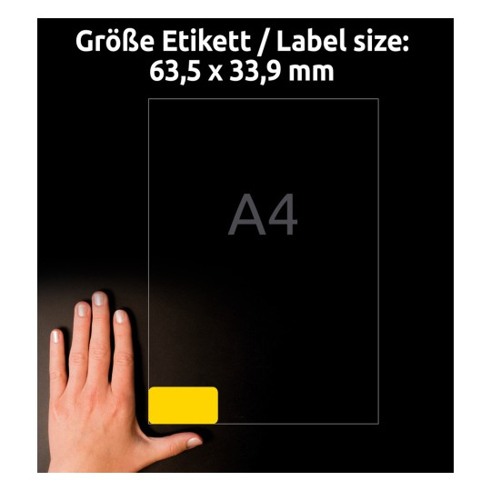Kuvassa näkyy käsi, joka on asetettu A4-arkin viereen, jossa on keltainen tarra alakulmassa. Tarran koko on 63,5 x 33,9 mm.