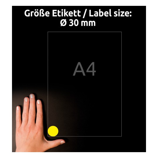 Kuvassa on käsi, joka on sijoitettu A4-kokoisen paperin viereen. Paperin alakulmassa on pyöreä keltainen tarra, jonka halkaisija on 30 mm. Tausta on tumma, mikä parantaa näkyvyyttä.