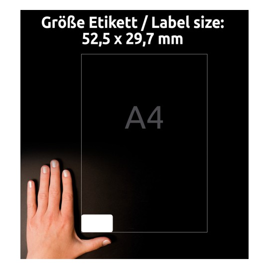 Kuva näyttää henkilön käden etiketin vieressä, jonka mitat ovat 52,5 x 29,7 mm, osoittaen etiketin koon. Käsi on sijoitettu etiketin vasempaan alakulmaan, ja koko on esitetty näkyvästi yläpuolella saksaksi ja englanniksi.