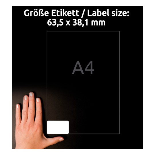 Kuva näyttää käden pitelevän A4-arkkia, jossa on merkitty etikettikoko 63,5 x 38,1 mm. Tausta on musta, ja teksti on saksaksi: 'Größe Etikett / Label size'.