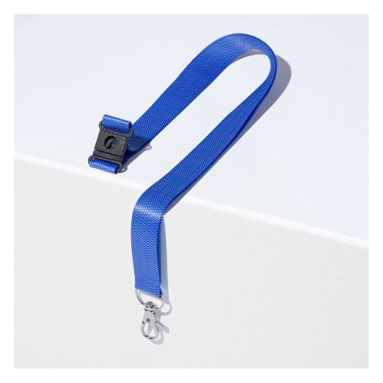 Kuvassa on sininen hihna, jossa on siksak-kuvio ja metallisolki. Se on asetettu valkoiselle pinnalle korostaen sen muotoilua ja väriä.