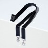 Kuvassa on musta hihna, jonka toisessa päässä on yksi klipsi ja toisessa päässä kaksi metalliklipsiä, lepäämässä vaalealla pinnalla.