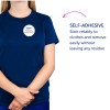 Kuvassa on henkilö, jolla on yllään laivastonsininen t-paita ja itseliimautuva nimikyltti, jossa lukee 'B. Carlos MARKKINOINTIJOHTAJA'. Oikealla oleva teksti korostaa itseliimautuvan ominaisuuden luotettavuutta ja sen jäämätöntä poistamista.