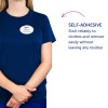 Kuvassa on henkilö, joka pukeutunut laivastonsiniseen paitaan ja nimikylttinä lukee 'B. Carlos, markkinointijohtaja.' Heidän vieressään on teksti, joka kuvailee itsekiinnittyvän ominaisuuden, joka tarttuu vaatteisiin ja irtoaa helposti jättämättä jäämiä.