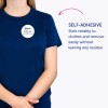 Kuvassa on henkilö, jolla on yllään sininen t-paita ja itseliimautuva nimikyltti, jossa lukee 'B. Carlos, markkinointijohtaja'. Teksti korostaa, että kyltti pysyy luotettavasti vaatteissa ja sen voi poistaa helposti jättämättä jälkiä.
