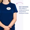 Kuvassa on henkilö, joka käyttää sinistä paitaa, jonka päällä on itseliimautuva nimikyltti, jossa lukee 'B. Carlos, markkinointijohtaja.' Tekstissä korostetaan kyltin liimaominaisuutta, joka takaa luotettavan pysyvyyden ja mahdollisuuden poistaa kyltin ilman jäämiä.